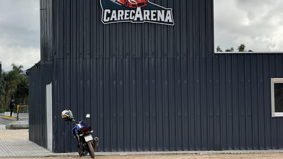 Estacionamento da CarecArena em frente ao barracão, com moto estacionada sob o logo da pista.
